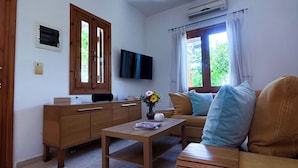 Una sala de estar con un sofá de madera, una mesa de centro, un televisor de pantalla plana y una ventana con cortinas.