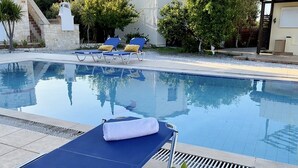 Zona junto a la piscina con sillas de descanso, una mesa con bebidas y una vista despejada de la piscina.