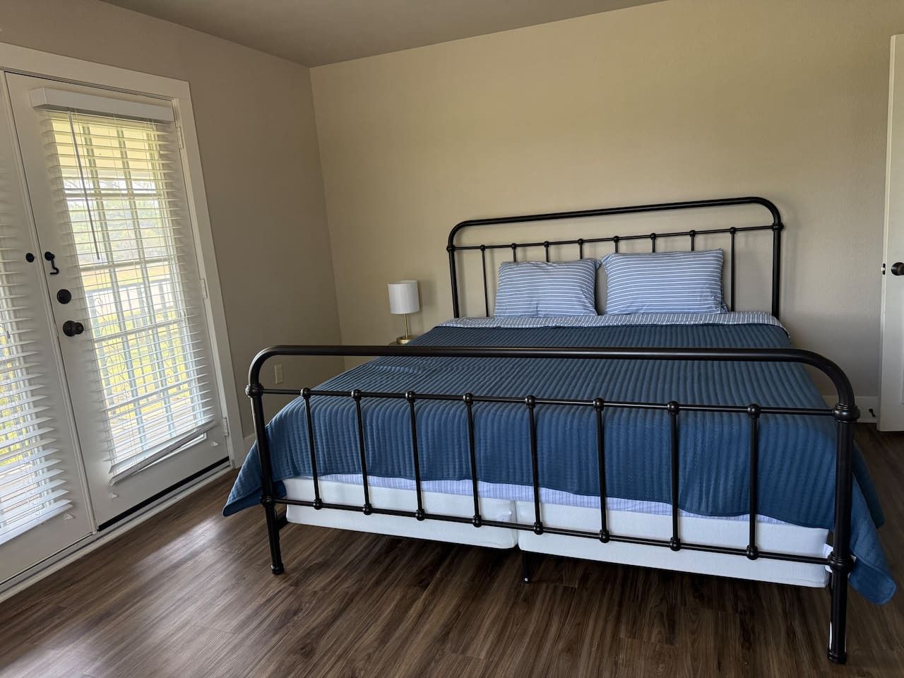Une chambre à coucher avec un lit en métal, une couvre-lit à rayures bleues et une table de chevet blanche avec une lampe.