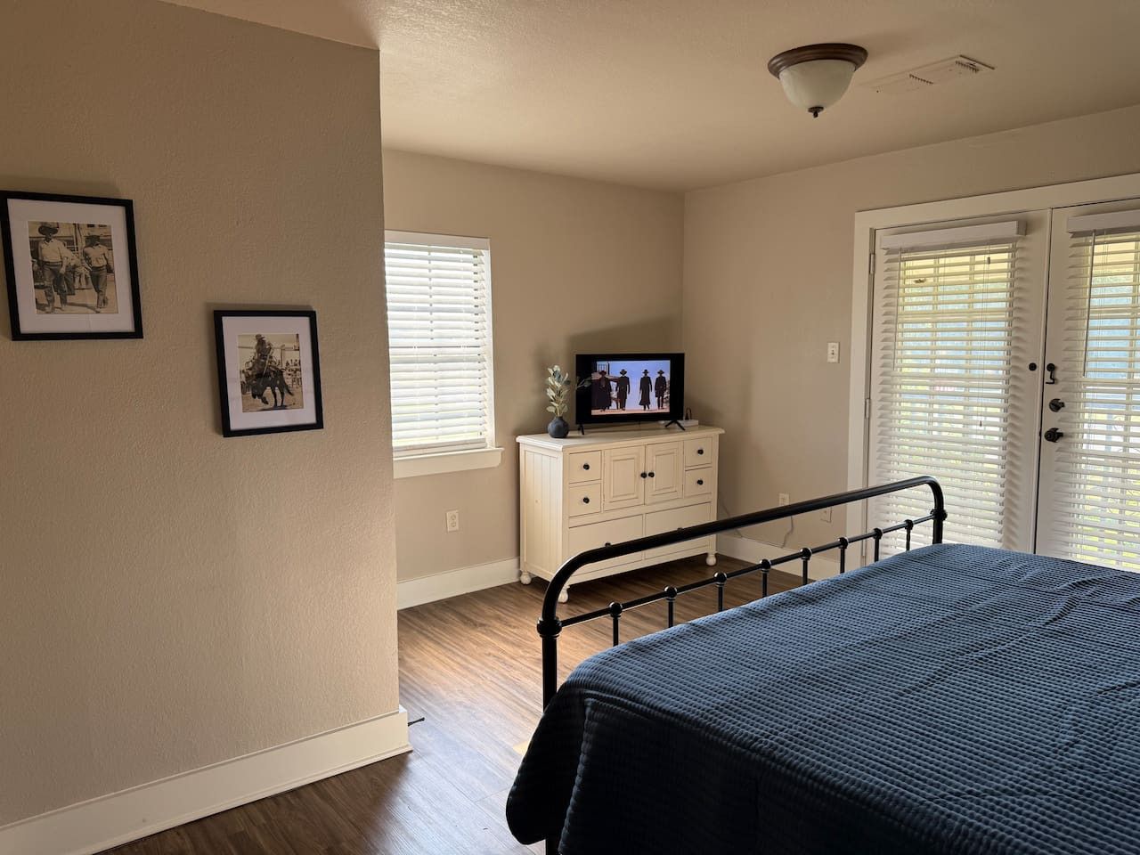 Une chambre à coucher avec un lit, une commode, un téléviseur posé sur la commode et deux tableaux encadrés accrochés au mur.