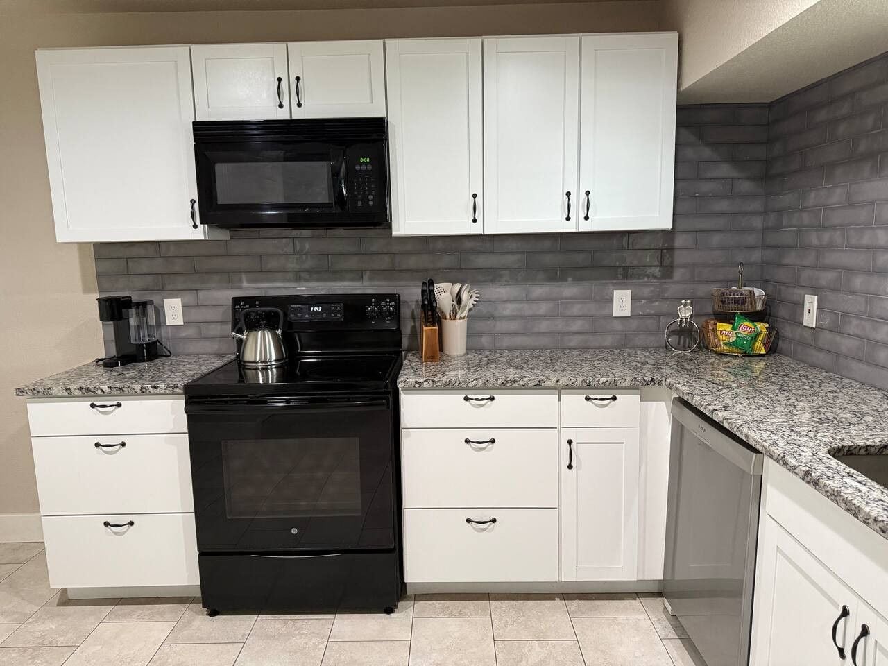 A modern kitchen with white cabinets, a black stove, and a granite countertop.