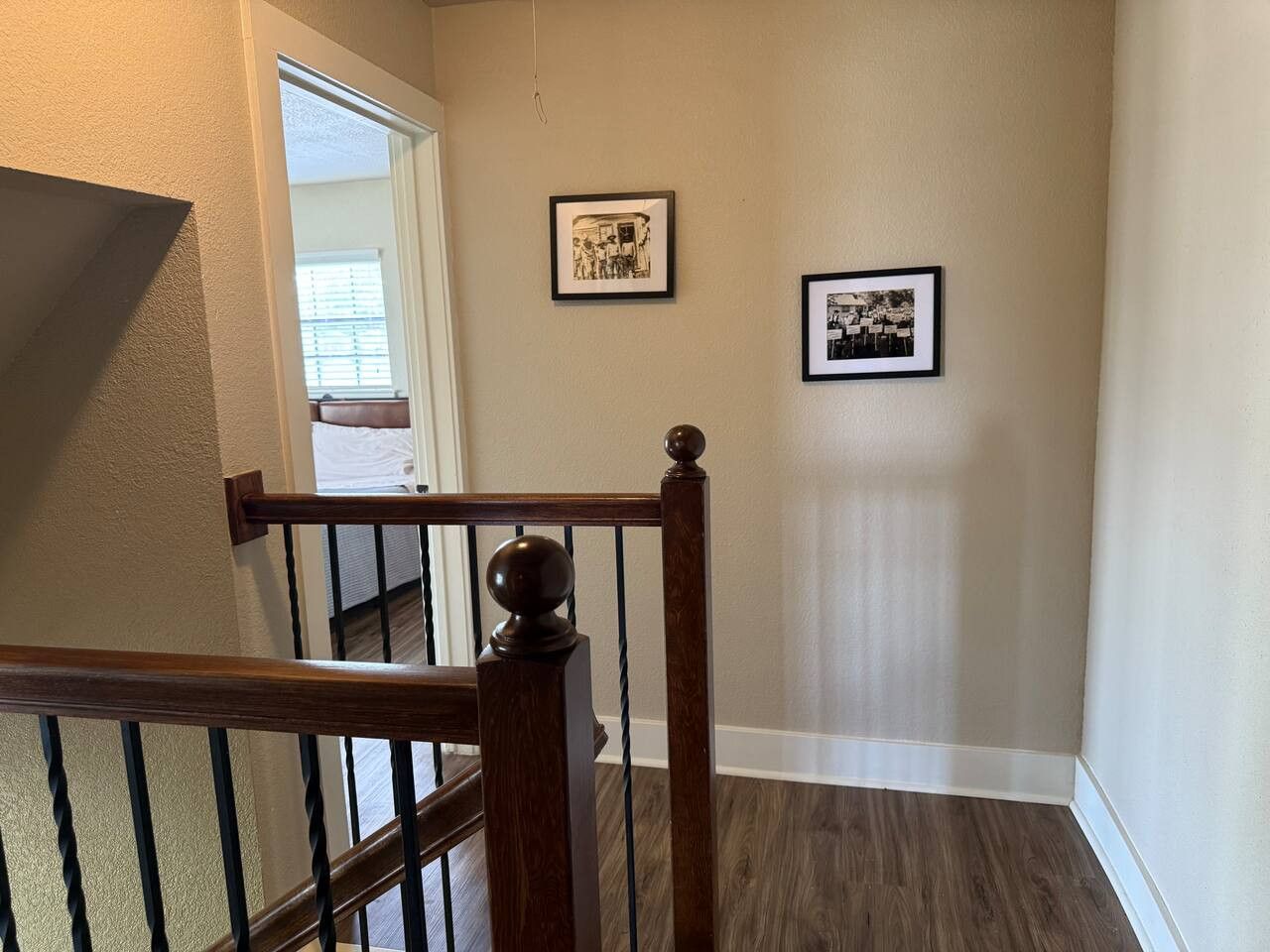 A staircase with a wooden handrail and black balusters, leading to a room with beige walls and a dark wood floor.