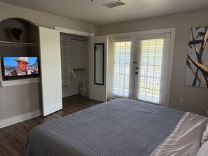 Un dormitorio con una cama grande, un televisor montado en la pared, un vestidor y una puerta corrediza de vidrio al exterior.
