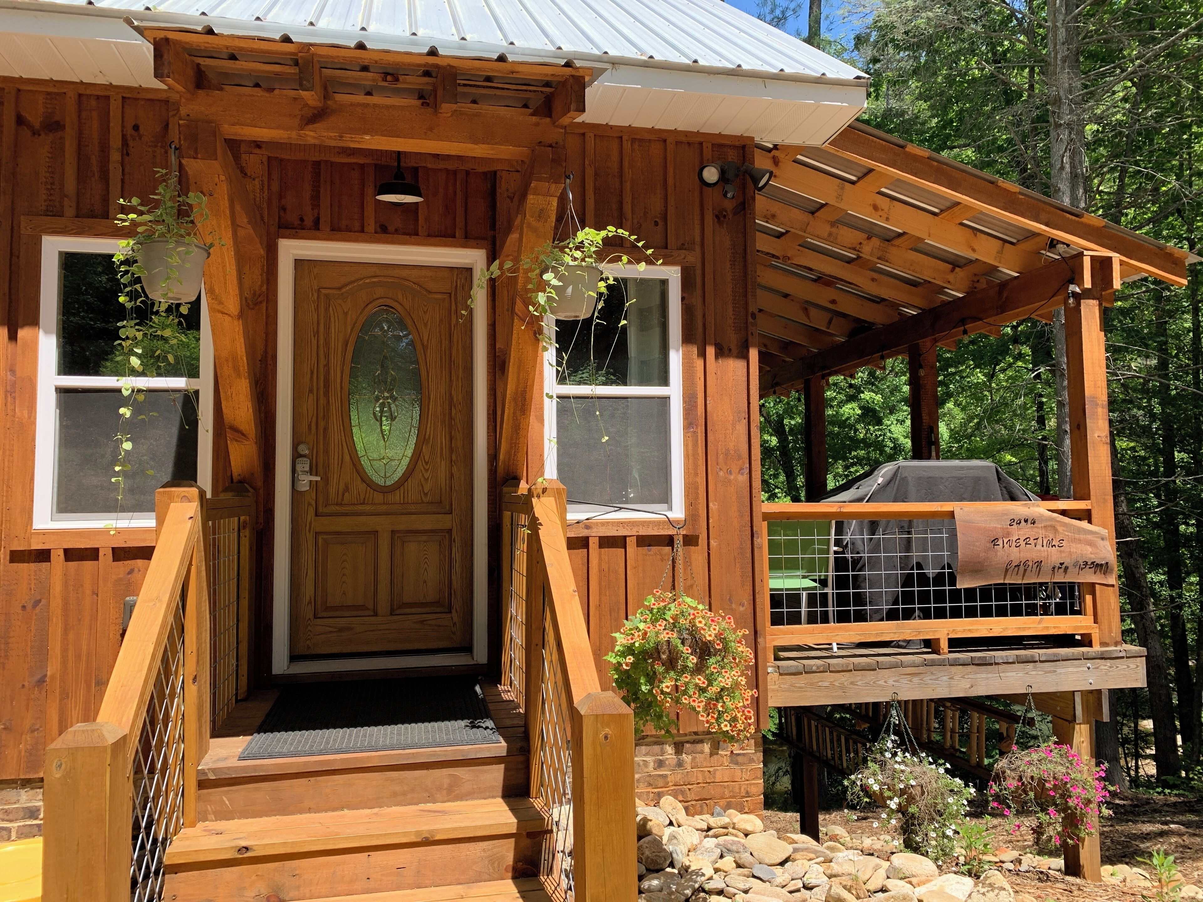 Une cabane en bois dotée d’un porche couvert, d’un espace barbecue et d’un chemin de pierre menant à l’entrée.
