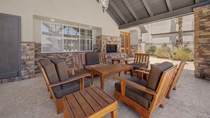 An outdoor patio with wooden furniture, a stone fireplace, and a covered ceiling. - Modern 2BR/2BA Retreat: Ground Floor / Pool, Spa, Gym / North Scottsdale Getaway (Scottsdale)