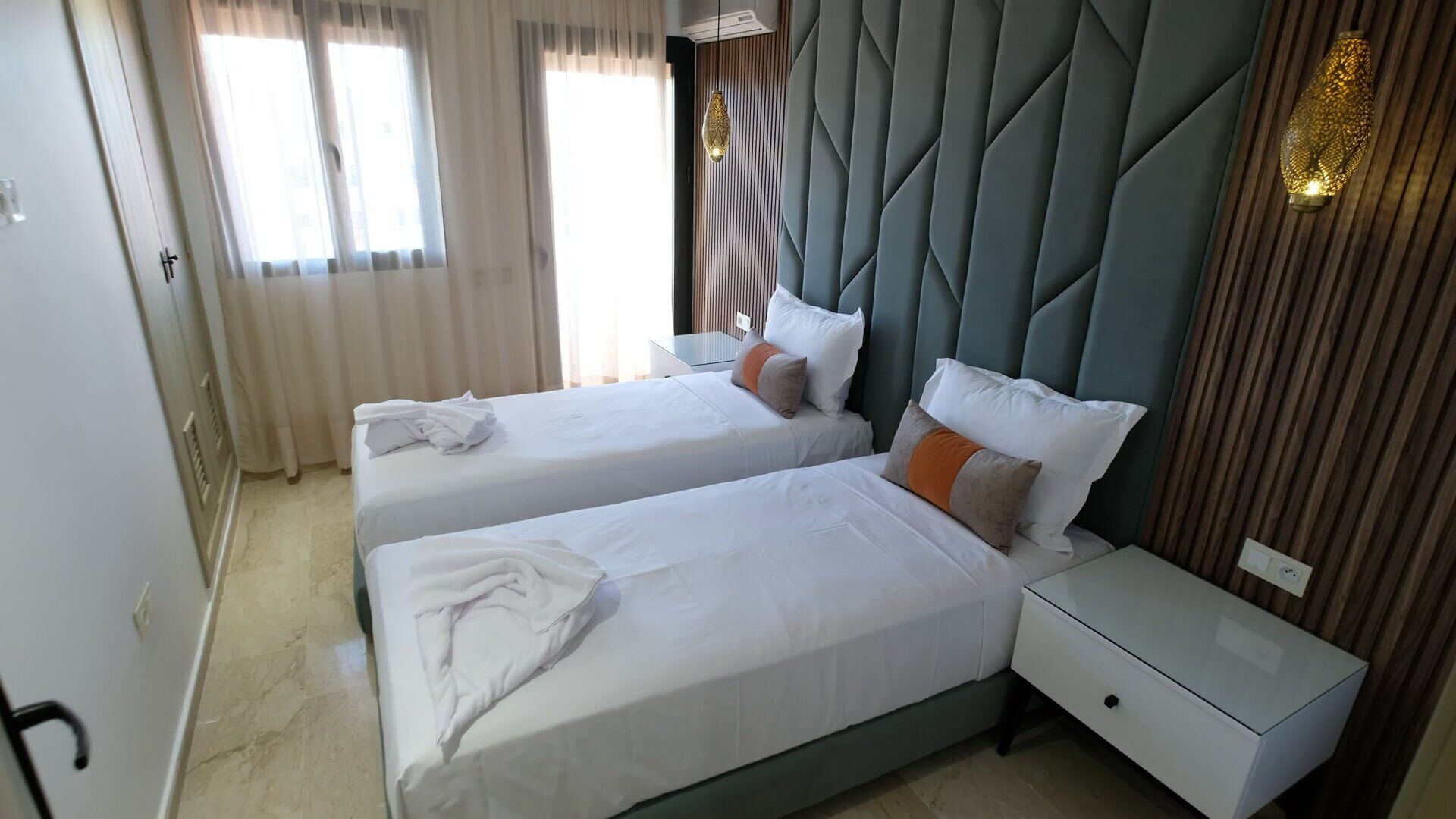 A hotel room with two beds, a nightstand, a dresser, and a window with curtains.