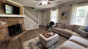 A living room with a stone fireplace, a staircase, a beige sofa, and a ceiling fan. - Spacious double units dublex in Lawrenceville (Lawrenceville)
