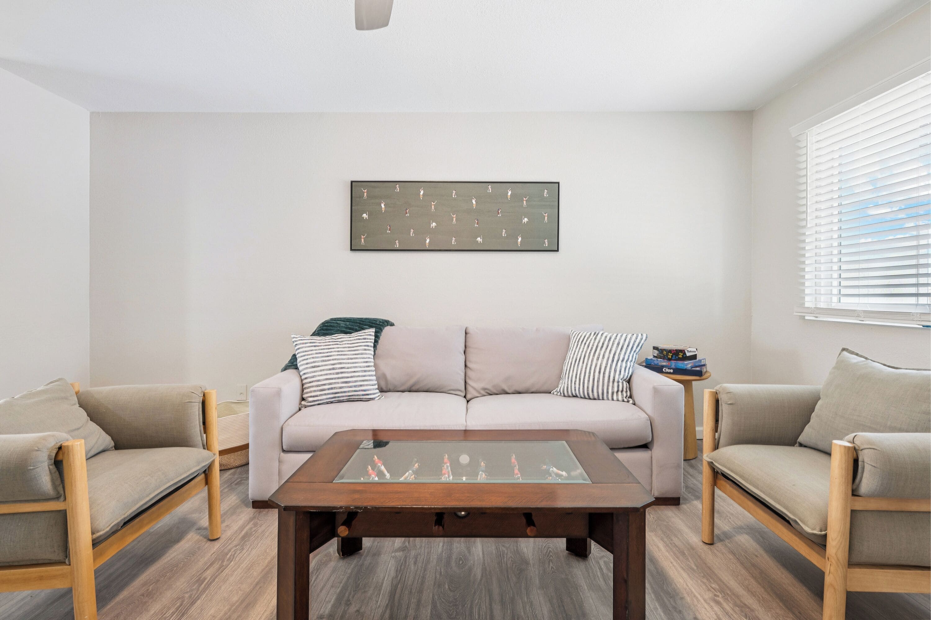 A living room with a beige sofa, two armchairs, a glass-top coffee table, and a wall-mounted artwork.