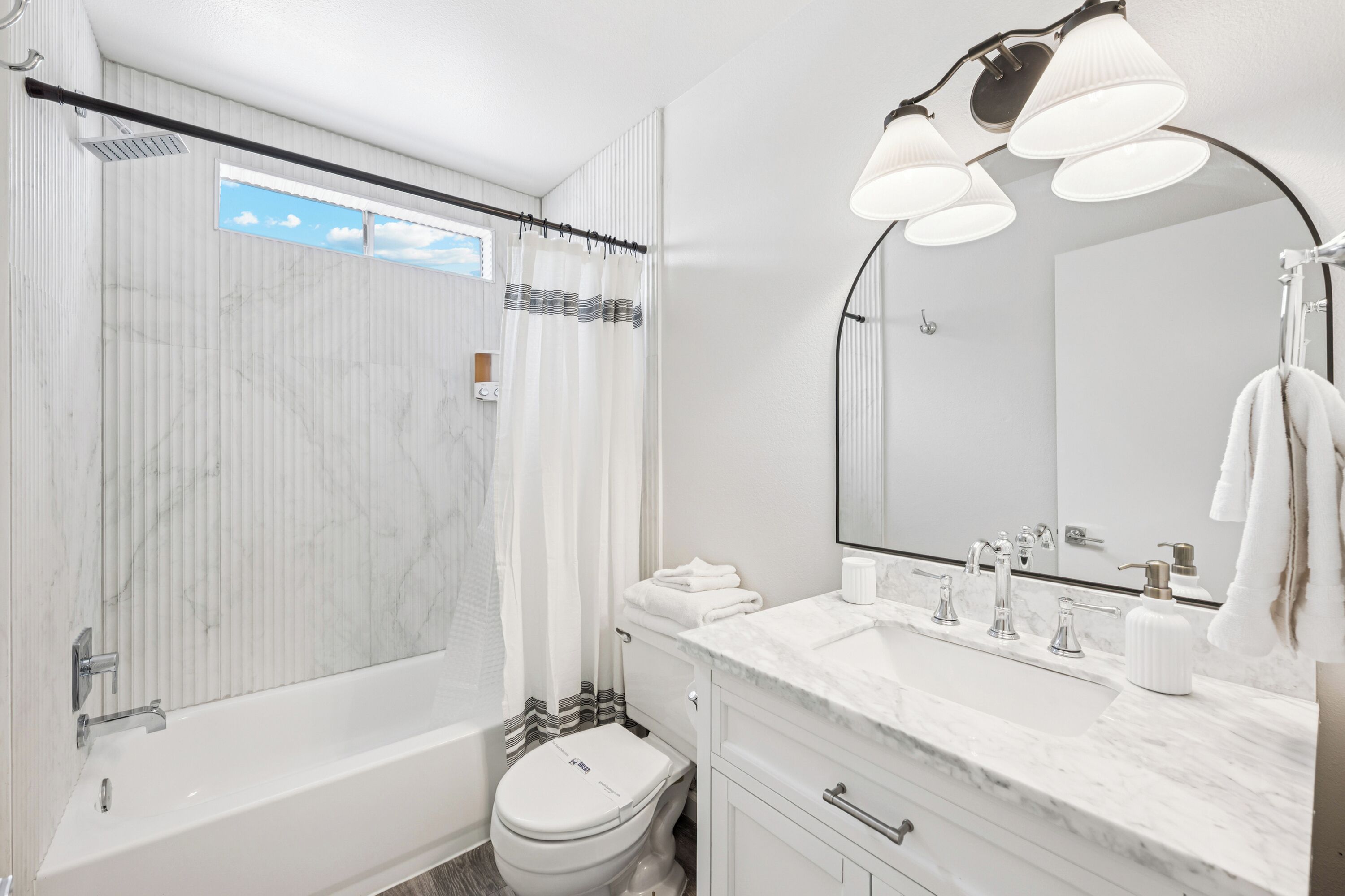 A modern bathroom with a bathtub, toilet, and vanity with a large mirror.
