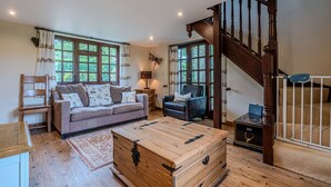Una sala de estar acogedora con una escalera de madera, un sofá, un sillón y un gran cofre de madera.