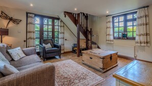 Un salón acogedor con sofá, sillón, cómoda de madera y una escalera.