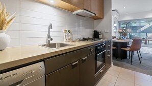 A modern kitchen with stainless steel appliances, a built-in oven, and a dining area with a round table and chairs. - The Inkerman Hideaway (St Kilda)