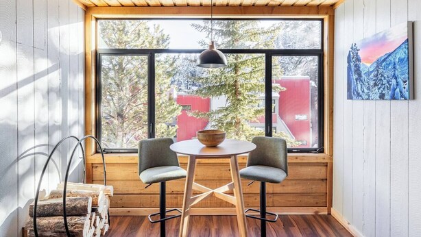A cozy room with a large window, two chairs, a table, and a hanging light fixture.
