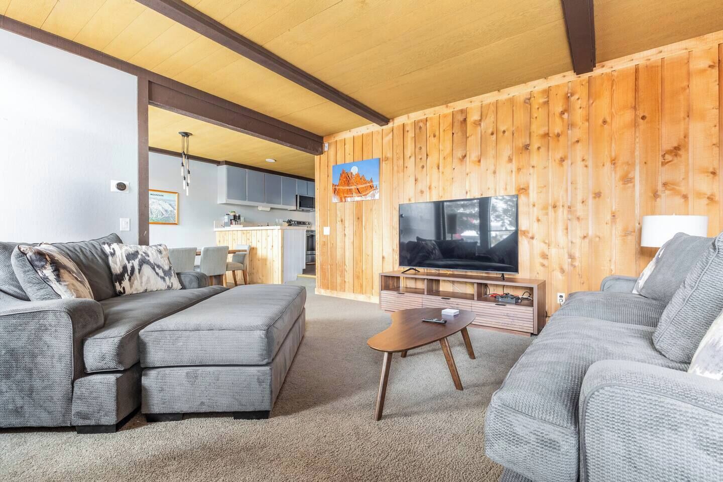 A modern living room with a large flat-screen TV, grey sofas, and a wooden accent wall.
