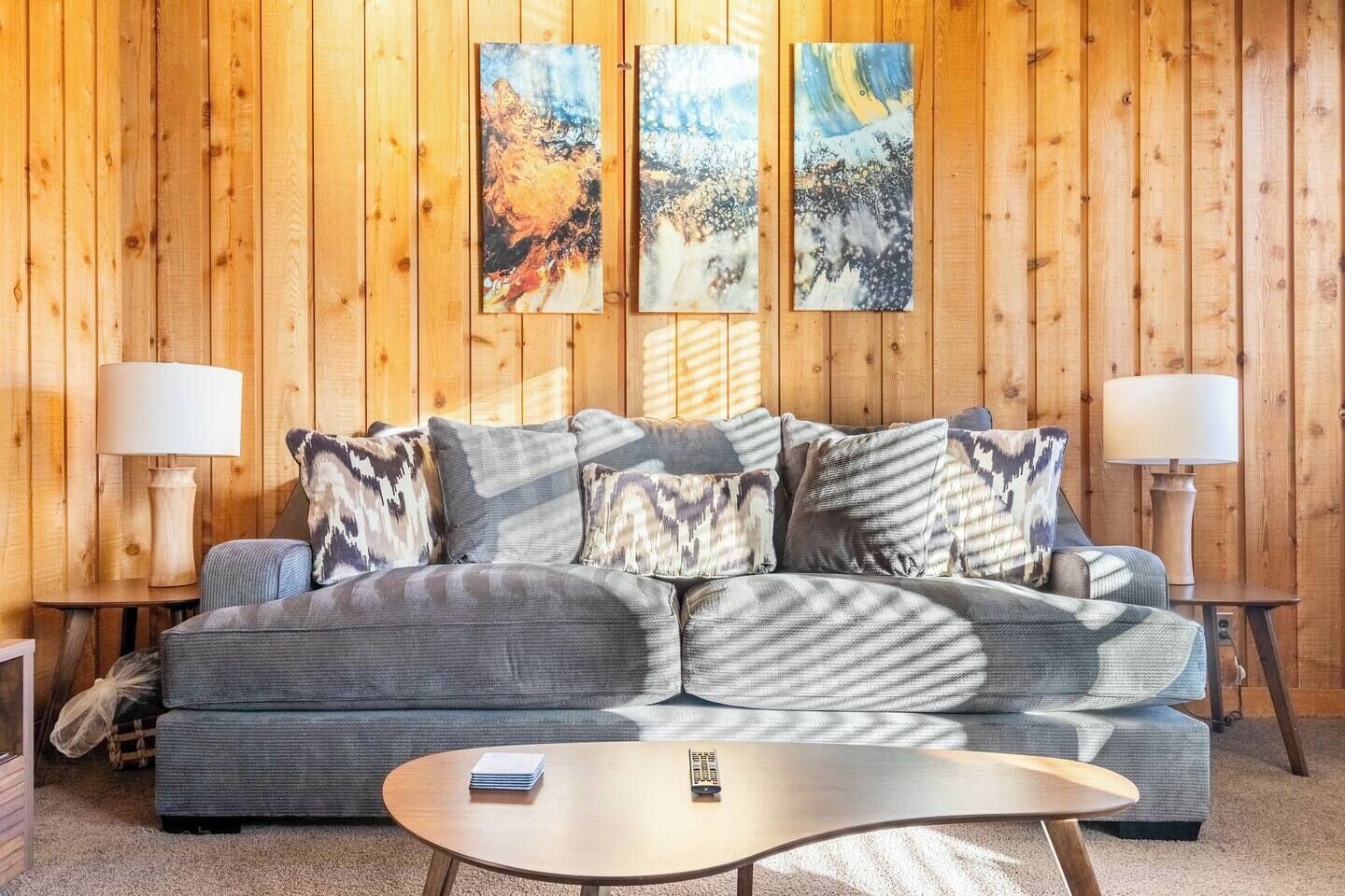 Una sala de estar con un sofá gris, cojines estampados, dos mesitas de noche con lámparas y paneles de madera en las paredes.