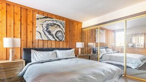 A bedroom with a wooden paneled wall, a large mirror, and a bed with a grey comforter.