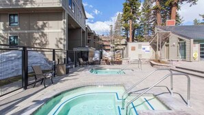 A pool area with two hot tubs, surrounded by a fence, and a building with a sign that reads "KIRKWOOD".
