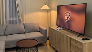 A modern living room with a sofa, a TV, a lamp, and a ceiling fan. - Amayara Nest Hospitality 2 BR Condo  (Cagayan de Oro)