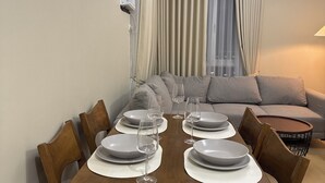 A dining area with a wooden table set for four, surrounded by chairs. There is a sofa and a lamp in the background. - Amayara Nest Hospitality 2 BR Condo  (Cagayan de Oro)