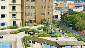 A swimming pool with a sun deck, surrounded by greenery and a view of residential buildings. - Amayara Nest Hospitality 2 BR Condo  (Cagayan de Oro)