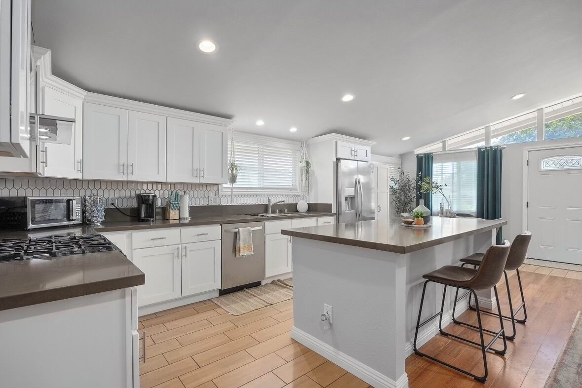 A modern kitchen with white cabinets, a central island, and a stainless steel refrigerator.