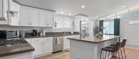 A modern kitchen with white cabinets, a central island, and a stainless steel refrigerator.