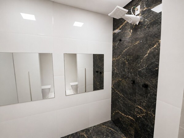 Une salle de bain moderne avec des carreaux blancs, un mur en marbre noir et une douche équipée d’un pommeau de douche à main.