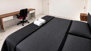 Un dormitorio con cama, escritorio, silla y una pequeña mesita de noche.