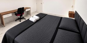 Un dormitorio con cama, escritorio, silla y una pequeña mesita de noche.