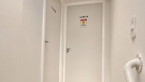 Un pasillo estrecho con una puerta cerrada, un letrero en la pared y una tubería blanca.