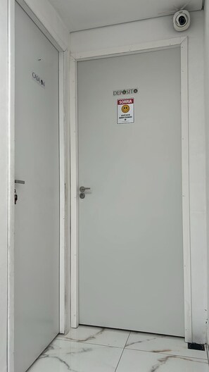 A white door with a deposit sign, a smiley face sign, and a security camera above it. - Aconchego de Lugar - Eri&Douglas (Belo Horizonte)
