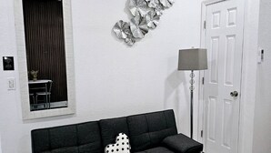 A modern living room with a black sofa, a decorative wall piece, a white door, and an air conditioning unit. - ROMANTIC SUITE MAYDUNY (Tampa)