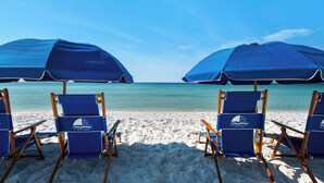 A beach with two blue umbrellas and four blue beach chairs.