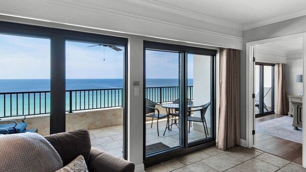 A balcony with a view of the ocean, a seating area with chairs and a table, and a door leading to a room.