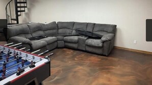 A room with a gray sectional sofa, a foosball table, and a spiral staircase. - Bedrooms for rent in a very nice space (Joplin)