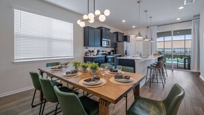 A modern kitchen with dark cabinets, a wooden dining table set with plates, glasses, and a plant. - WI3277 - 5BR house near Disney with private pool (Davenport)