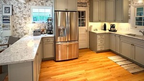 A kitchen with a large stainless steel refrigerator, light green cabinets, a marble countertop, and wooden flooring. - 328 Cherry Close Walk to Downtown and Pool (Lakeside)