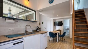 Une cuisine moderne équipée d’un lave-vaisselle encastré, d’un évier et d’un plan de travail en bois. On y trouve également un coin repas avec une table et des chaises, ainsi qu’un téléviseur fixé au mur.