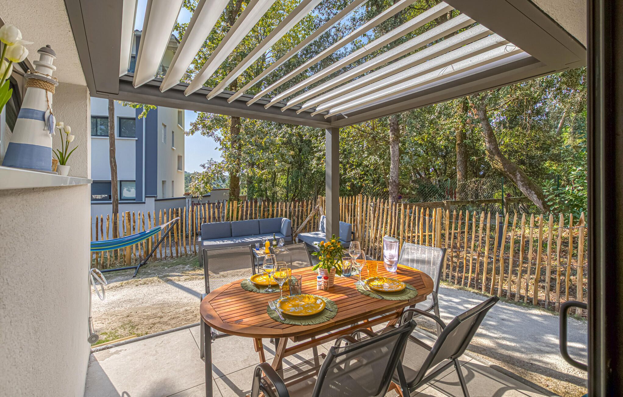 Eine Terrasse im Freien mit einem Holztisch, gedeckt für ein Essen, einer Hängematte und einem blauen Sofa.