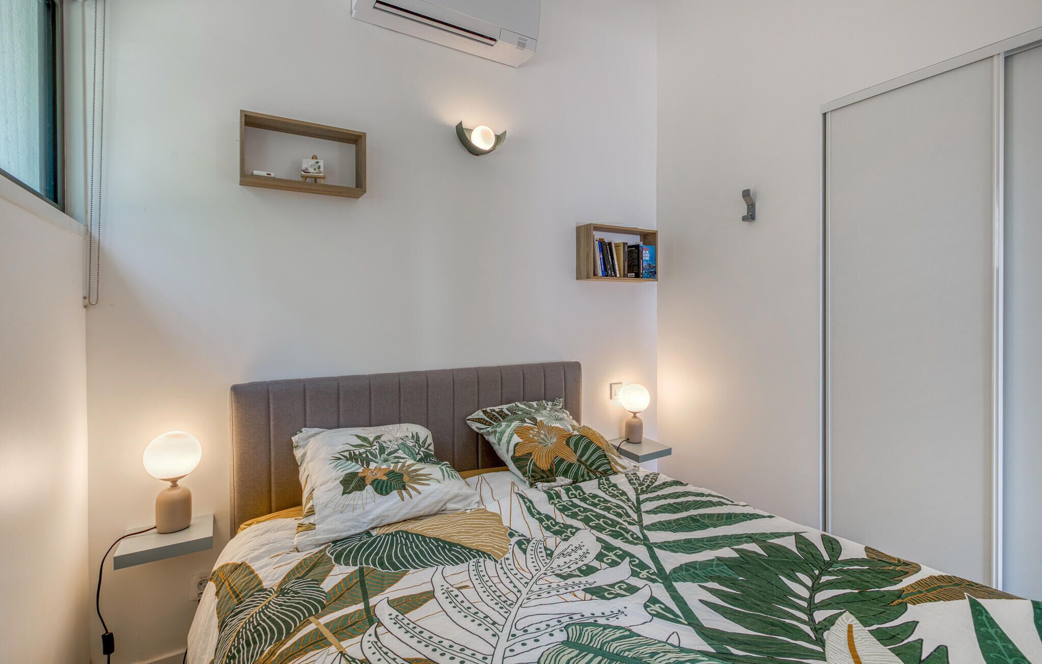 Een slaapkamer met een bed, nachtlampen, een wandplank met boeken en een klein decoratief object.
