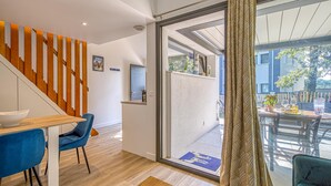 Un intérieur moderne avec un escalier en bois, un coin repas avec des chaises bleues et une vue sur l’extérieur grâce à une porte vitrée.