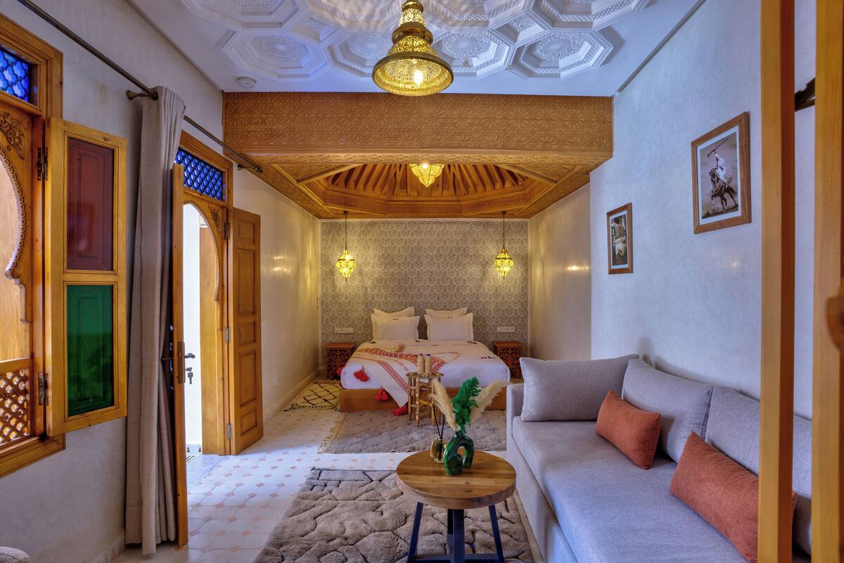 A bedroom with a bed, a sofa, a small table, and a decorative vase.