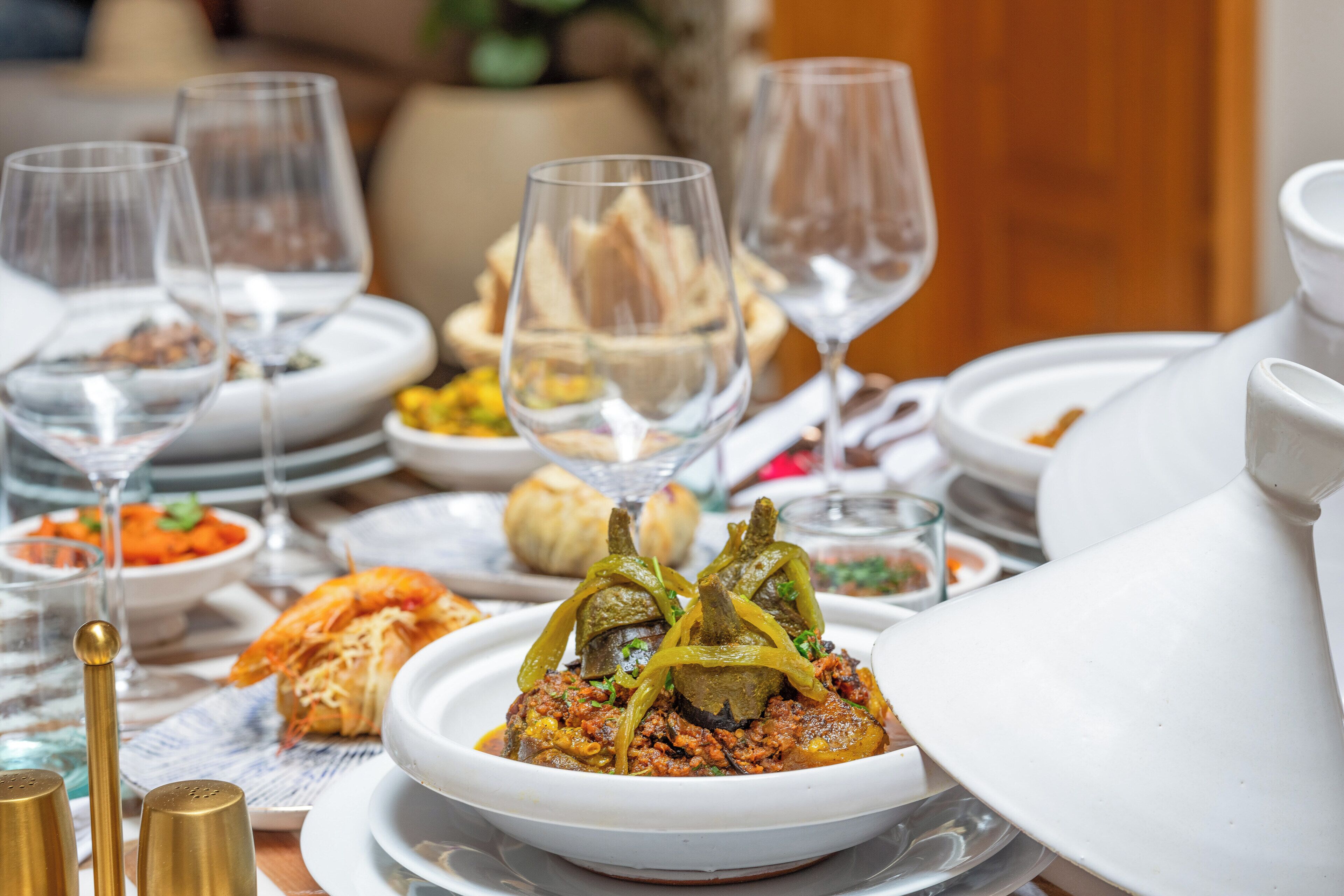 Una mesa de comedor dispuesta con diversos platos, incluyendo un plato central con verduras rellenas, rodeada de fuentes y copas.