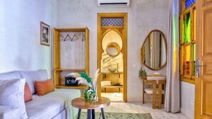 A living room with a sofa, a small round table, a mirror, and a door leading to a bathroom. - Riad Al Ghazlan  (Marrakech)