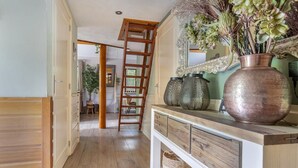 A hallway with a wooden floor, a wooden ladder, a white console table with decorative vases, and a mirror with an ornate frame. - Gorgeous home in Erm with WiFi (Erm)
