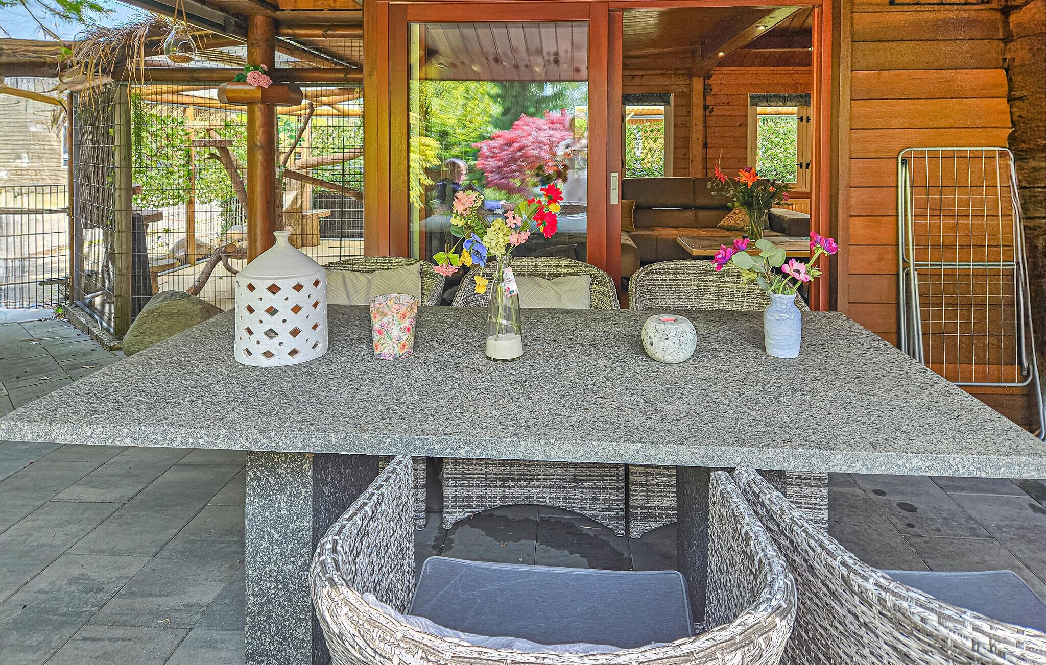 A covered outdoor seating area with a table set for dining, wicker chairs, and a view of the surrounding garden.