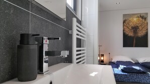 Un bany modern amb un lavabo blanc, un vas de color negre i un suport per a tovalloles.