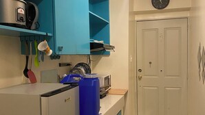 Una cocina compacta con armarios azul aguamarina, un refrigerador blanco, un microondas y un lavabo. Hay un reloj en la pared y una puerta a la derecha.