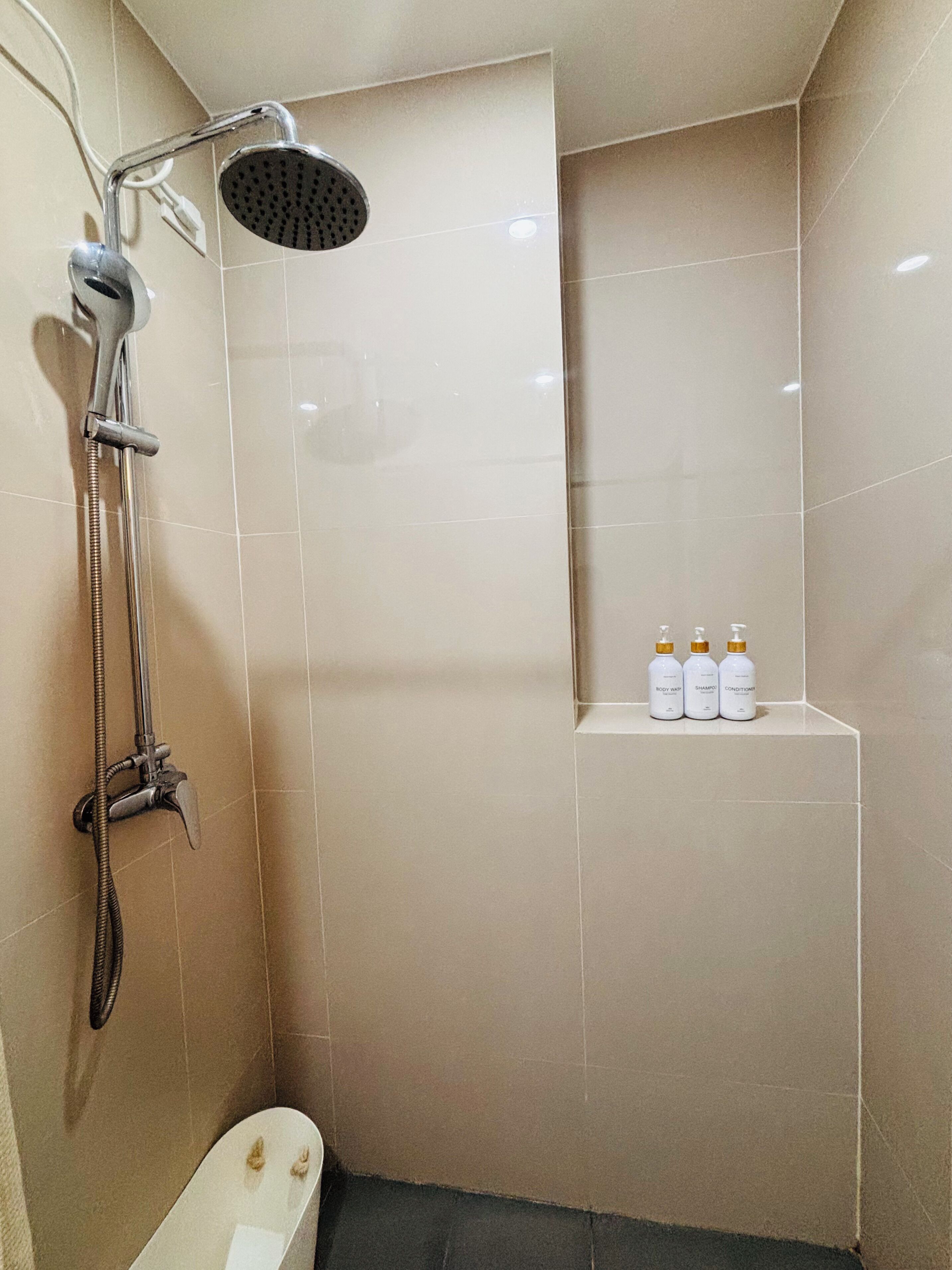 Ein Badezimmer mit Dusche, Toilette und einem Regal mit drei Flaschen.