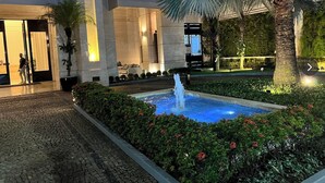 Un patio con fuente, zona de recepción y jardín cuidado con palmeras y arbustos.